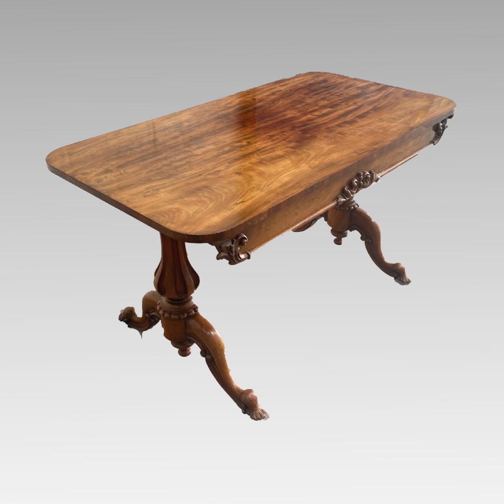 An early 19th-century mahogany library table with a polished rectangular top, carved aprons, and turned pedestal supports resting on scrolled feet. View III