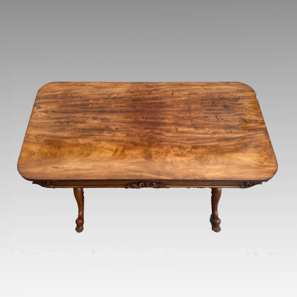 An early 19th-century mahogany library table with a polished rectangular top, carved aprons, and turned pedestal supports resting on scrolled feet. View V
