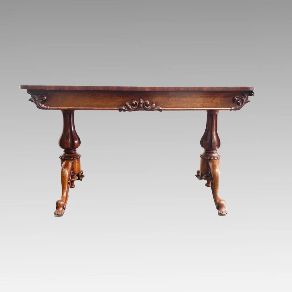 An early 19th-century mahogany library table with a polished rectangular top, carved aprons, and turned pedestal supports resting on scrolled feet. View VI