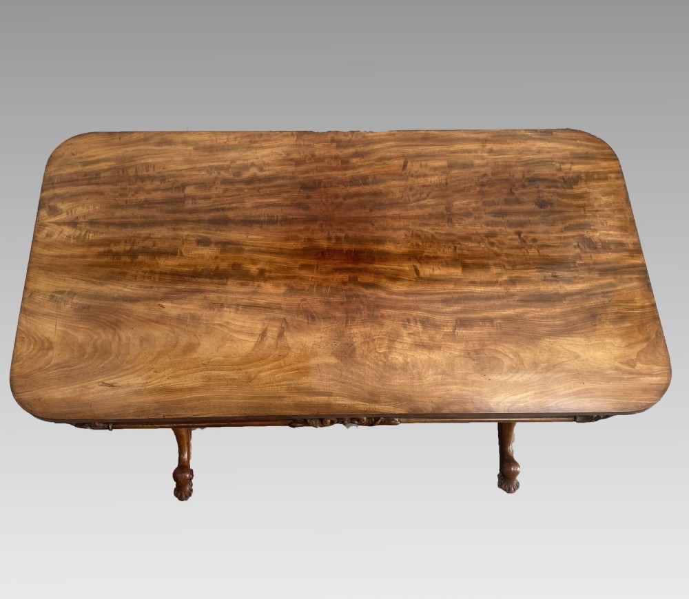 An early 19th-century mahogany library table with a polished rectangular top, carved aprons, and turned pedestal supports resting on scrolled feet. View VII