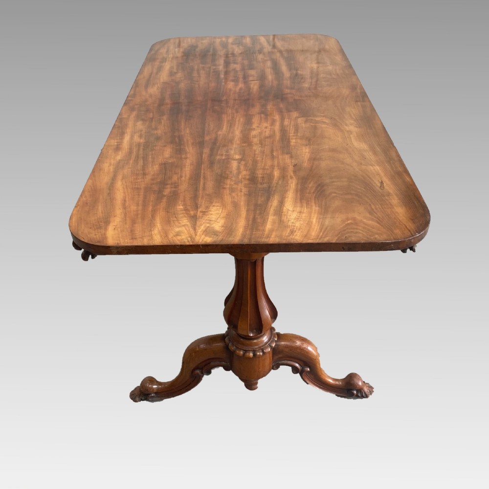 An early 19th-century mahogany library table with a polished rectangular top, carved aprons, and turned pedestal supports resting on scrolled feet. View VIII