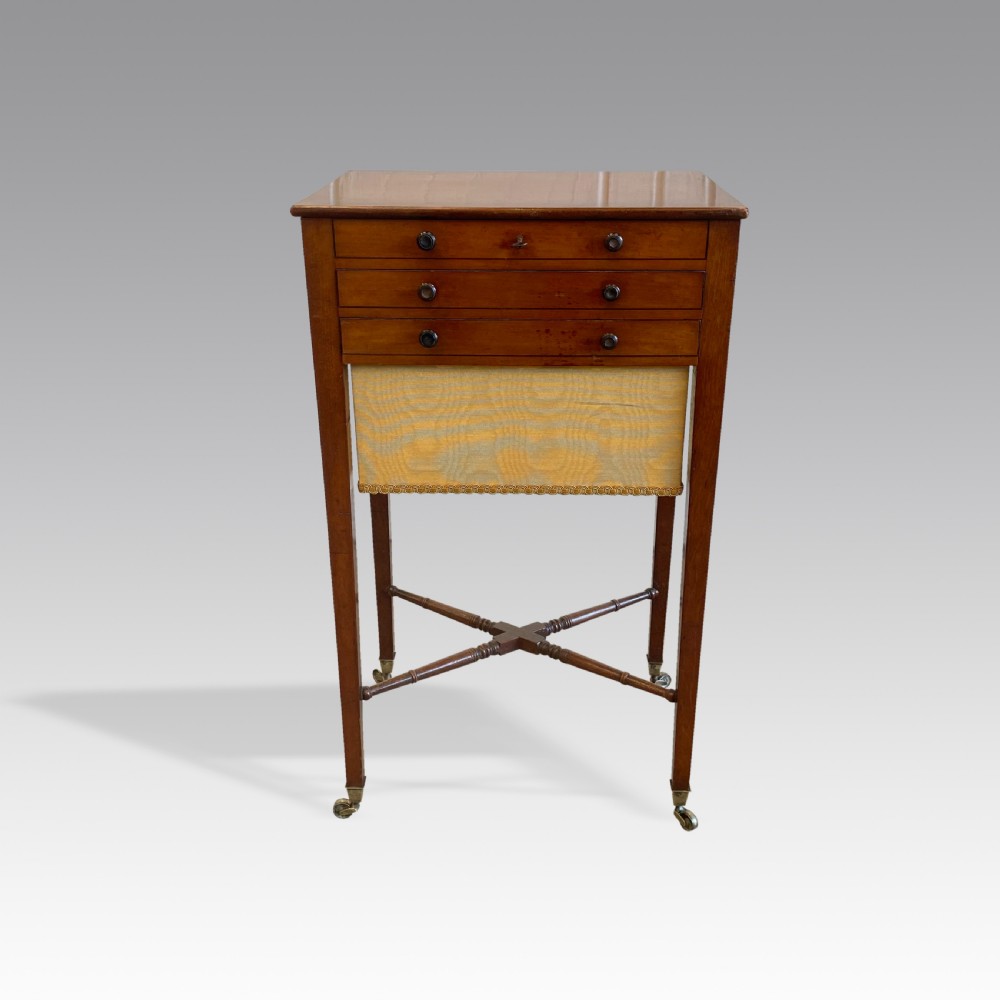 A Georgian mahogany needlework table featuring three drawers, a fabric work pouch, turned X-frame stretcher, and brass castors. View II