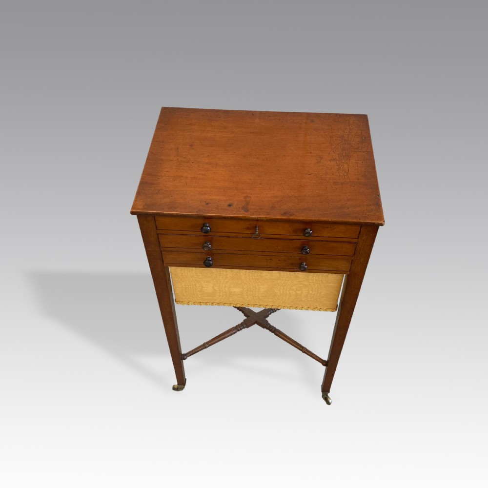 A Georgian mahogany needlework table featuring three drawers, a fabric work pouch, turned X-frame stretcher, and brass castors. View III