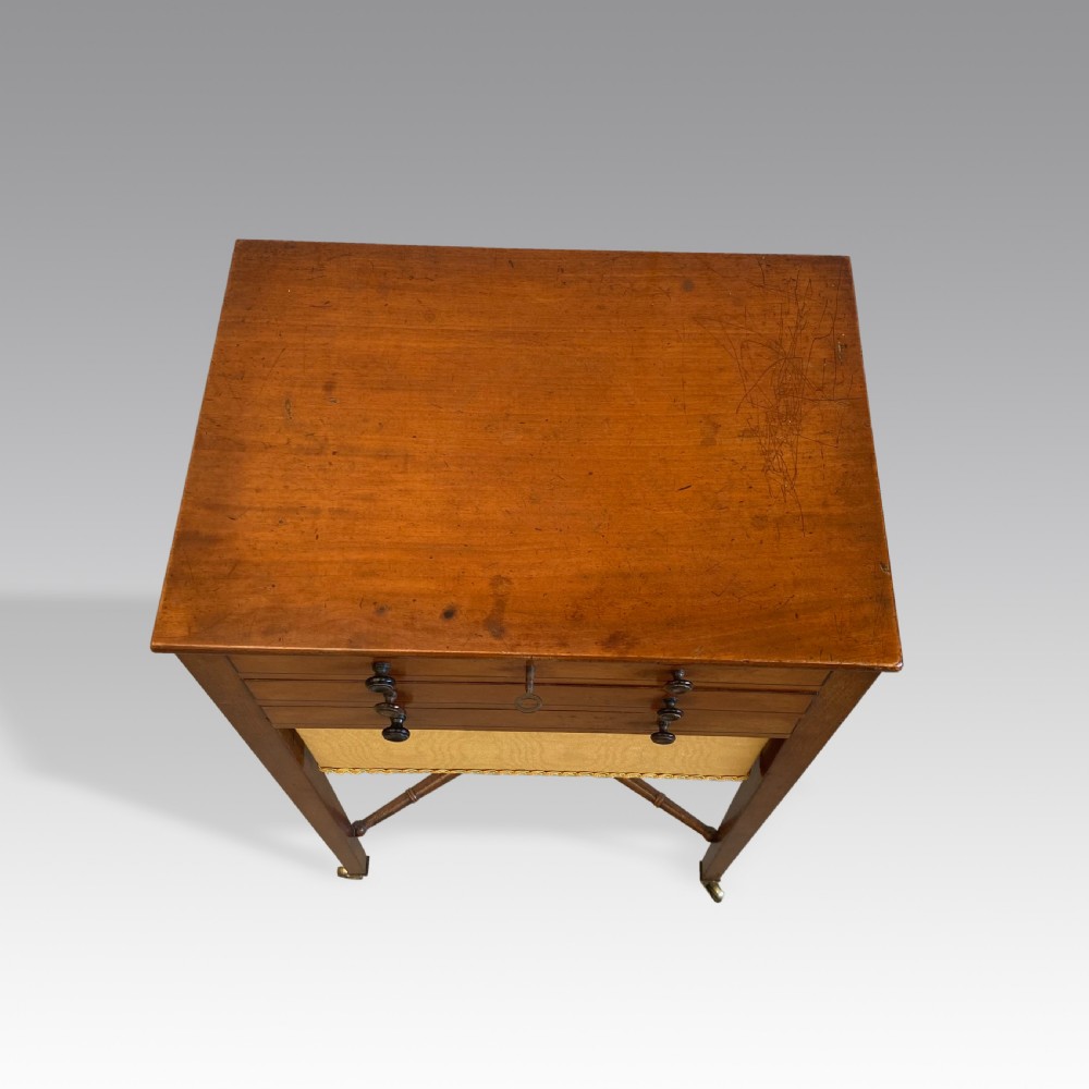A Georgian mahogany needlework table featuring three drawers, a fabric work pouch, turned X-frame stretcher, and brass castors. View IV