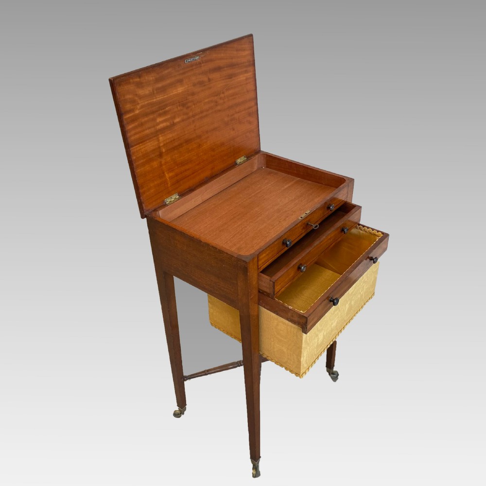 A Georgian mahogany needlework table featuring three drawers, a fabric work pouch, turned X-frame stretcher, and brass castors. View VII