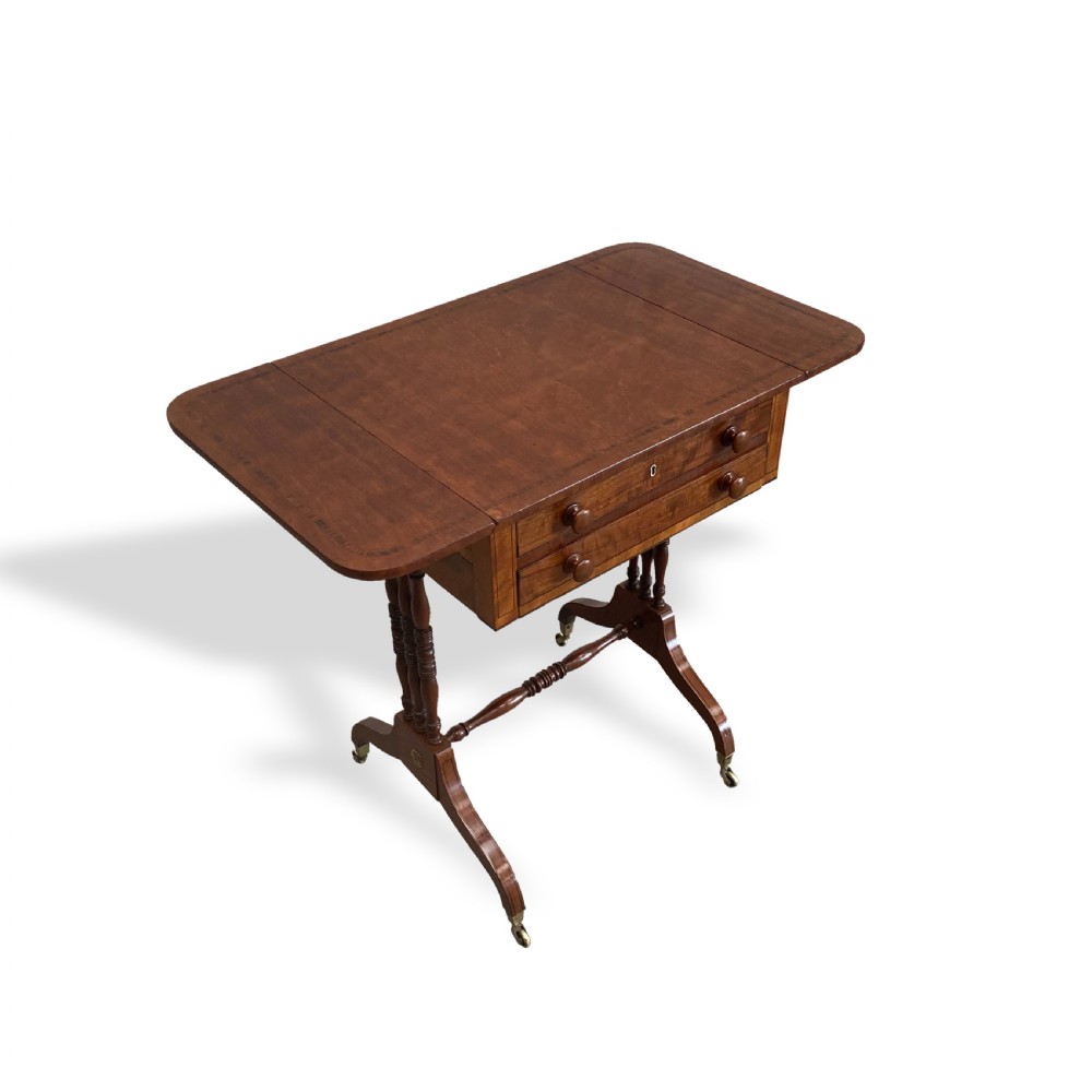 An antique Regency mahogany drop-flap occasional table featuring two drawers with wooden knobs, double turned upright pedestals, and splayed legs on brass castors. View III