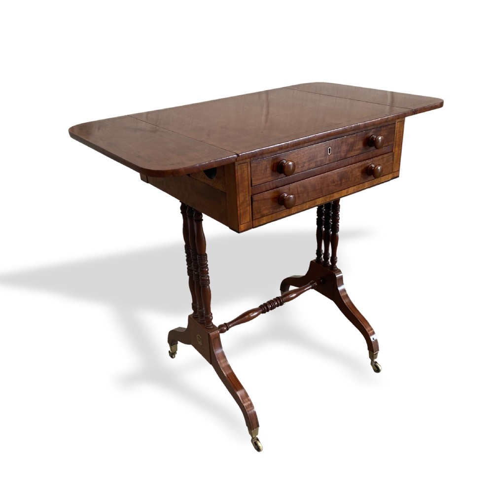 An antique Regency mahogany drop-flap occasional table featuring two drawers with wooden knobs, double turned upright pedestals, and splayed legs on brass castors. View IV
