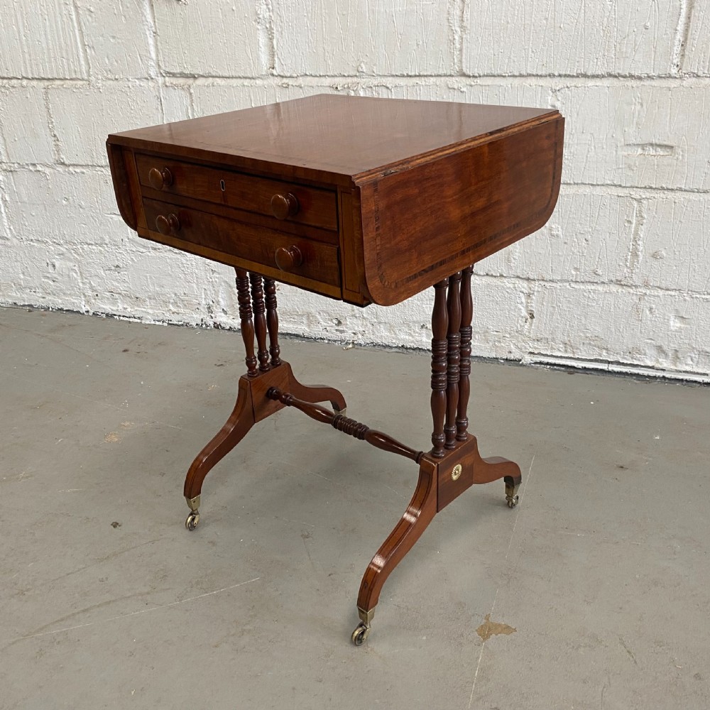 An antique Regency mahogany drop-flap occasional table featuring two drawers with wooden knobs, double turned upright pedestals, and splayed legs on brass castors. View VII