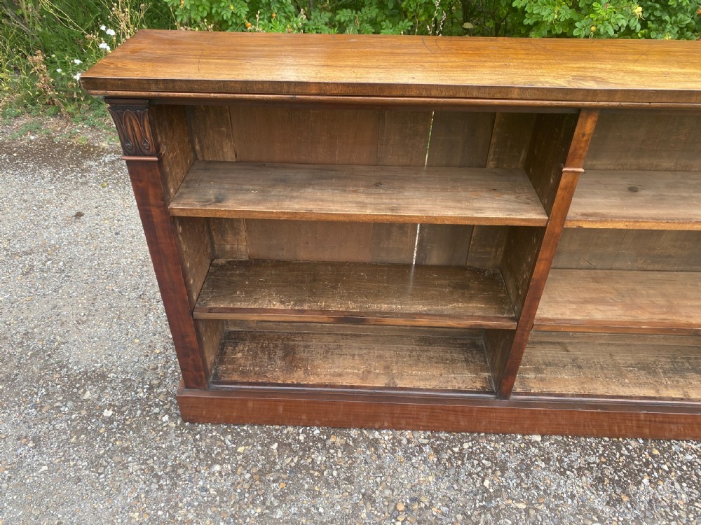 An English Regency mahogany low open bookcase featuring carved pilasters, adjustable shelves, and a solid plinth base. View V