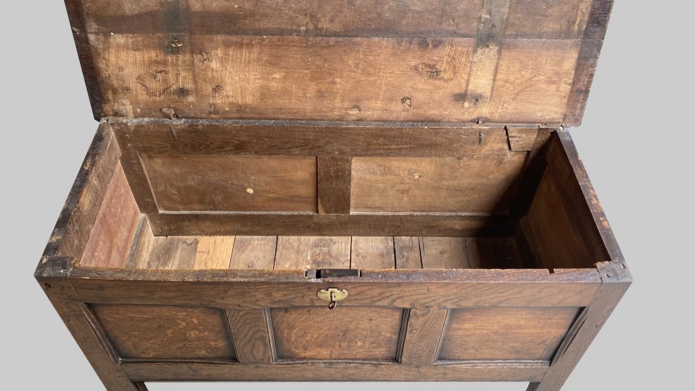 A seventeenth-century solid oak coffer featuring a hinged lid, three front panels, a central brass keyhole escutcheon, and square stile legs. View II