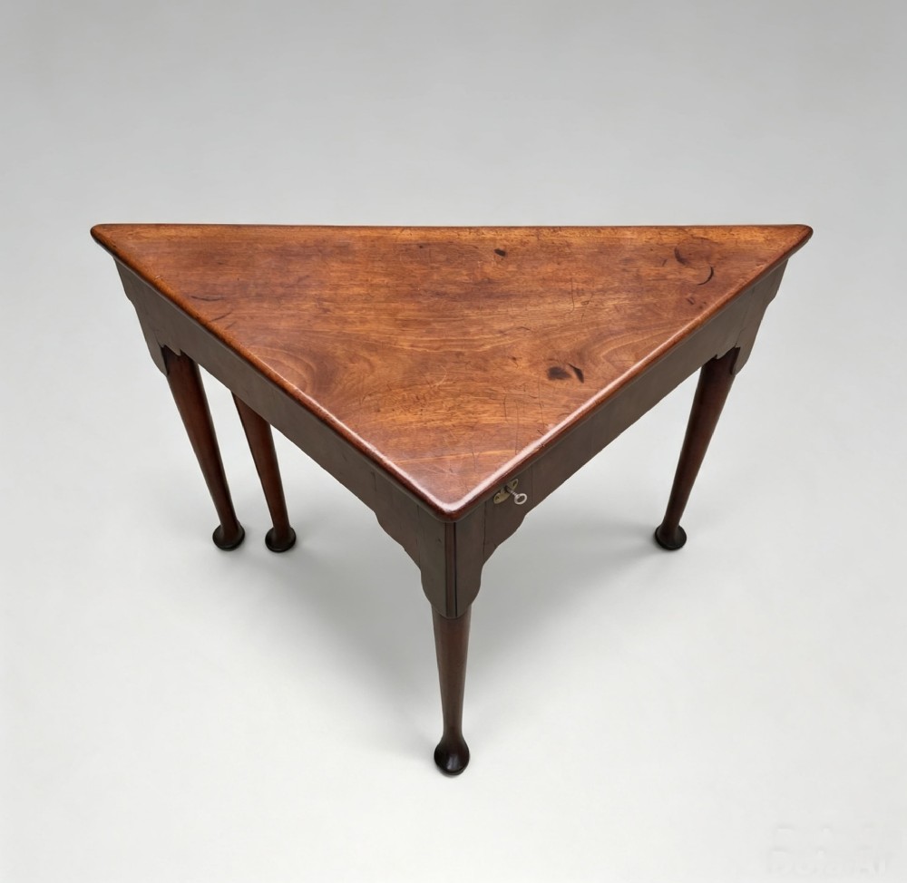 An 18th-century George II triangular mahogany handkerchief table featuring tapered turned legs terminating in pad feet and a keyhole frieze.
