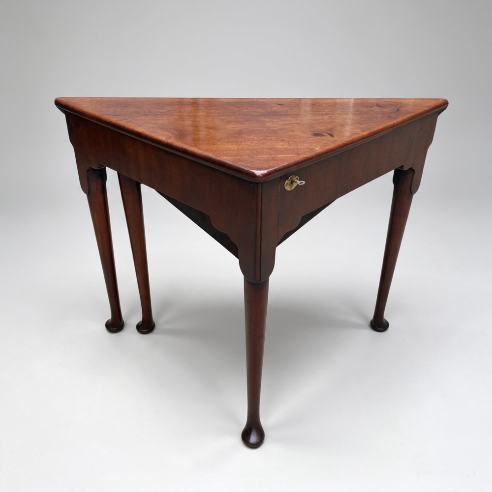An 18th-century George II triangular mahogany handkerchief table featuring tapered turned legs terminating in pad feet and a keyhole frieze. View X