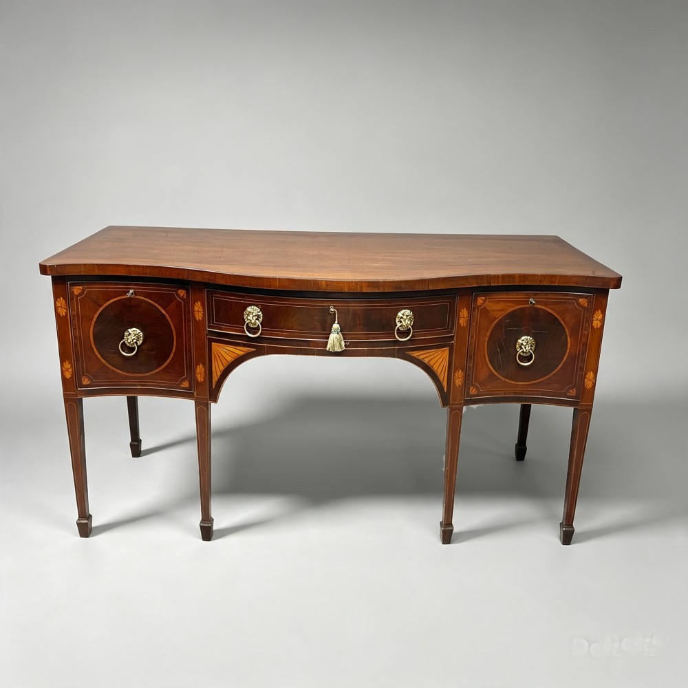 An antique mahogany serpentine-front sideboard featuring decorative wood inlays, brass lion-head ring handles, and square tapered legs. View II