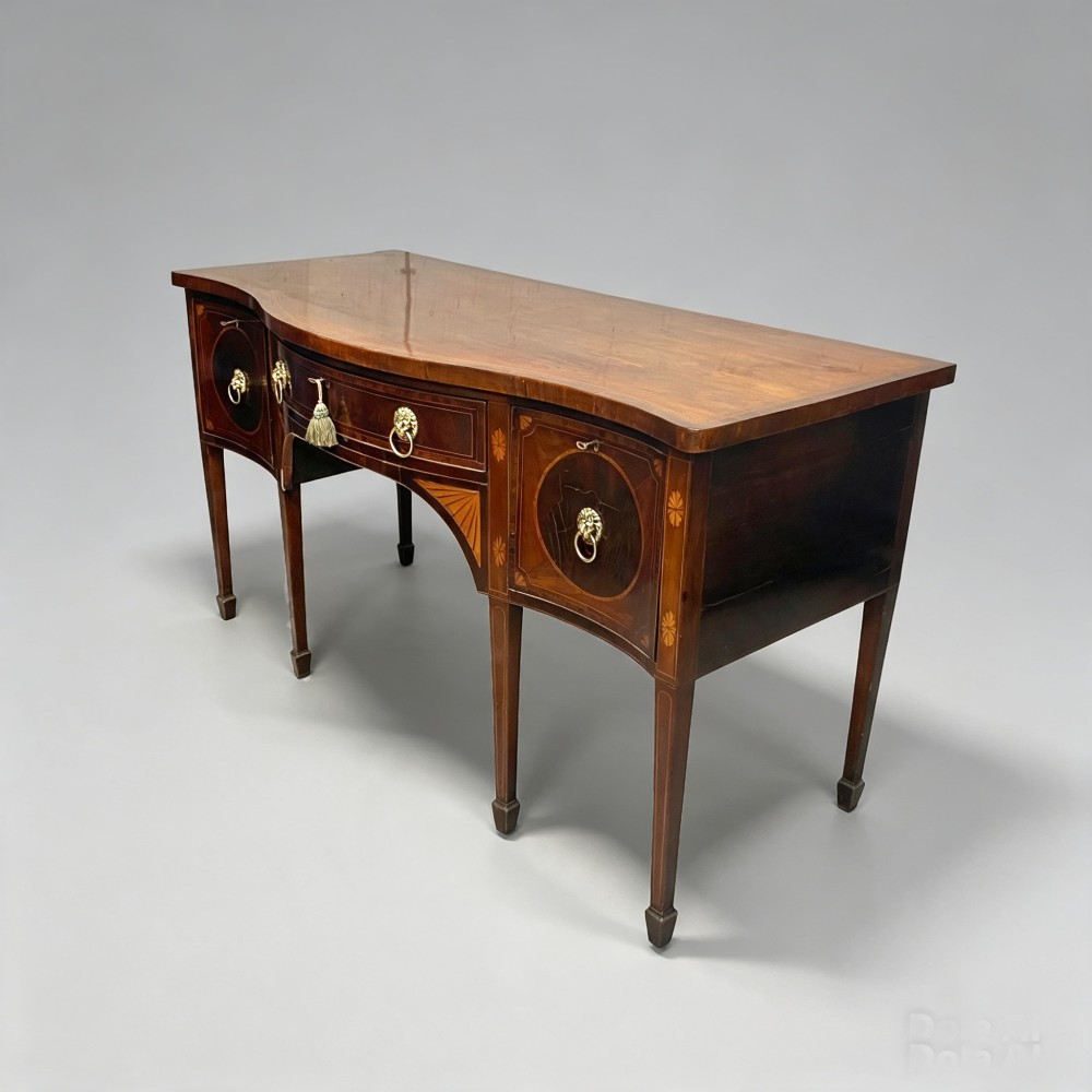 An antique mahogany serpentine-front sideboard featuring decorative wood inlays, brass lion-head ring handles, and square tapered legs. View V
