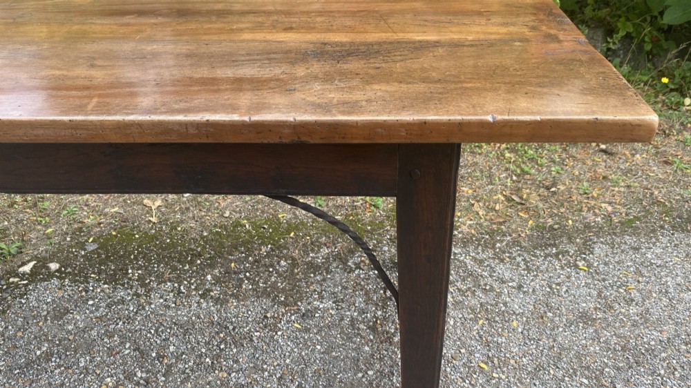 An antique rectangular refectory table made of warm fruitwood timber featuring a multi-plank top, dark legs, and metal corner support braces. View VII