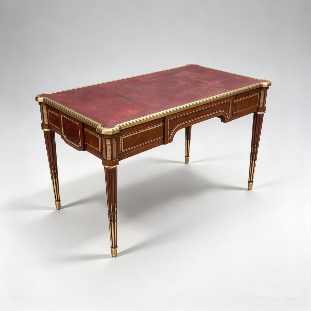 A French Napoleon III style mahogany bureau plat featuring a red leather inset top, gilt bronze mounts, three frieze drawers, and tapered fluted legs. View IV