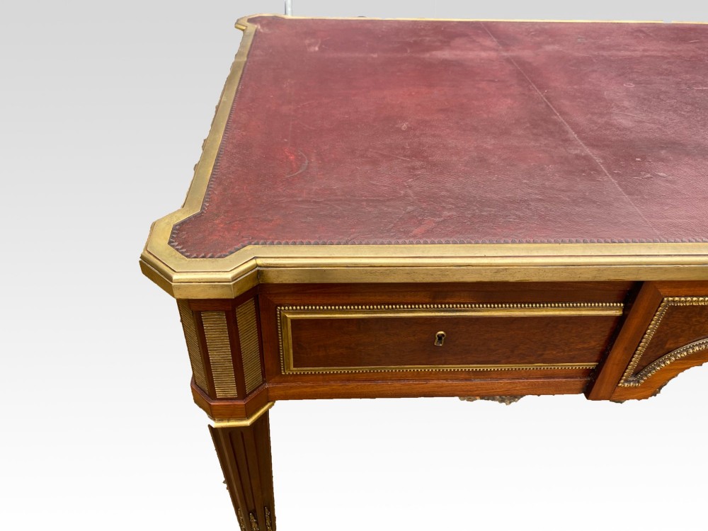 A French Napoleon III style mahogany bureau plat featuring a red leather inset top, gilt bronze mounts, three frieze drawers, and tapered fluted legs. View V