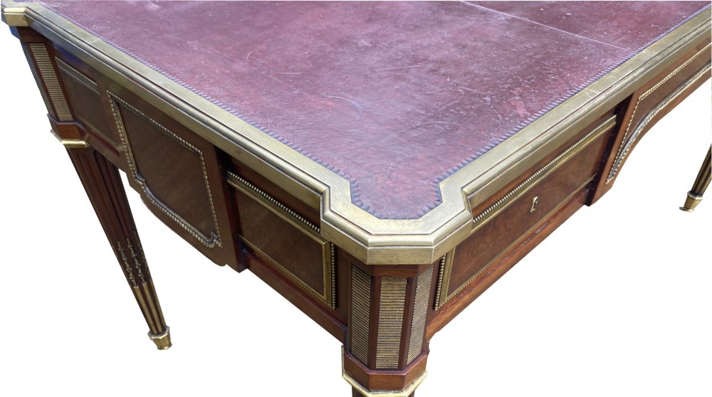 A French Napoleon III style mahogany bureau plat featuring a red leather inset top, gilt bronze mounts, three frieze drawers, and tapered fluted legs. View VI