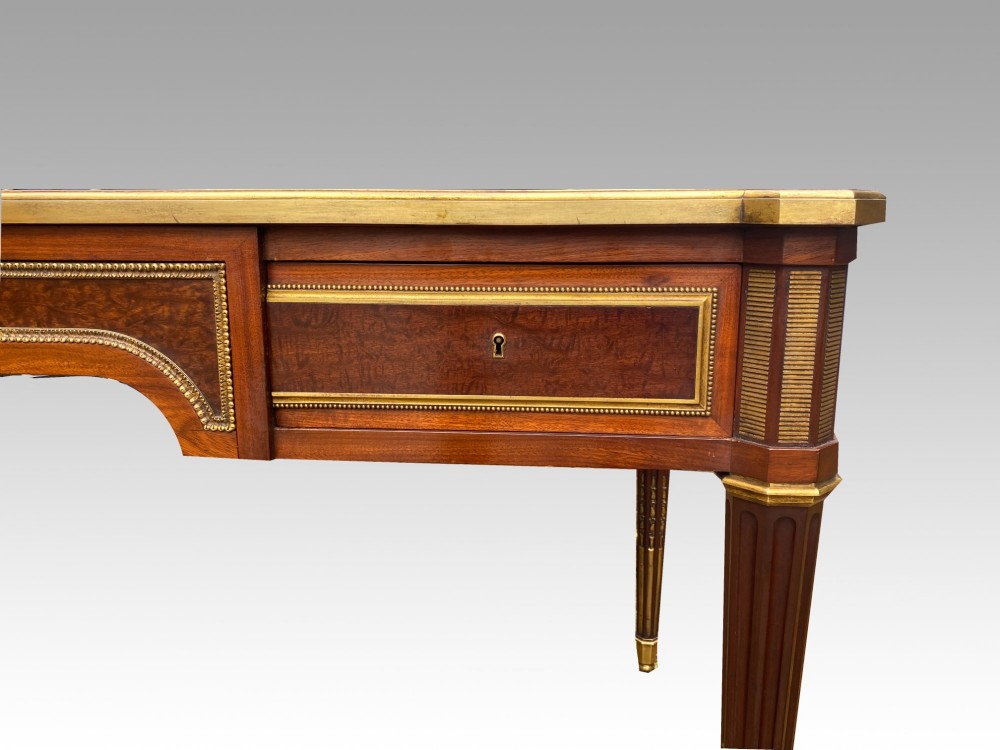 A French Napoleon III style mahogany bureau plat featuring a red leather inset top, gilt bronze mounts, three frieze drawers, and tapered fluted legs. View VIII