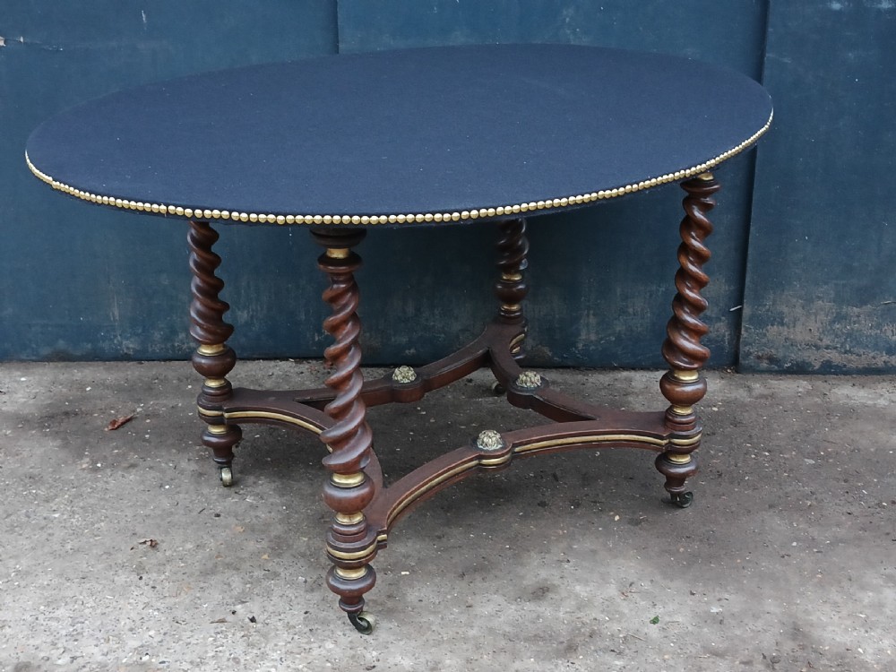 An oval antique gaming table featuring a dark baize top trimmed with brass studs, set upon barley-twist legs with a parcel-gilded stretcher base. View II