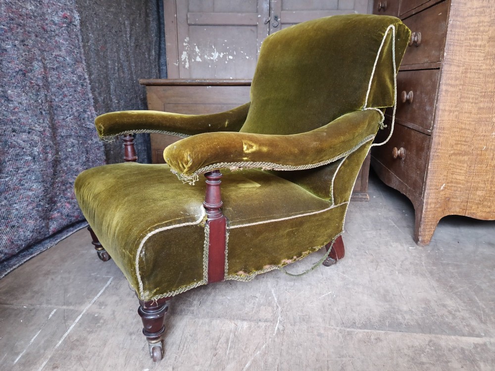 An antique Victorian low easy chair upholstered in olive green velvet with turned wooden arm supports and legs on brass castors. View II