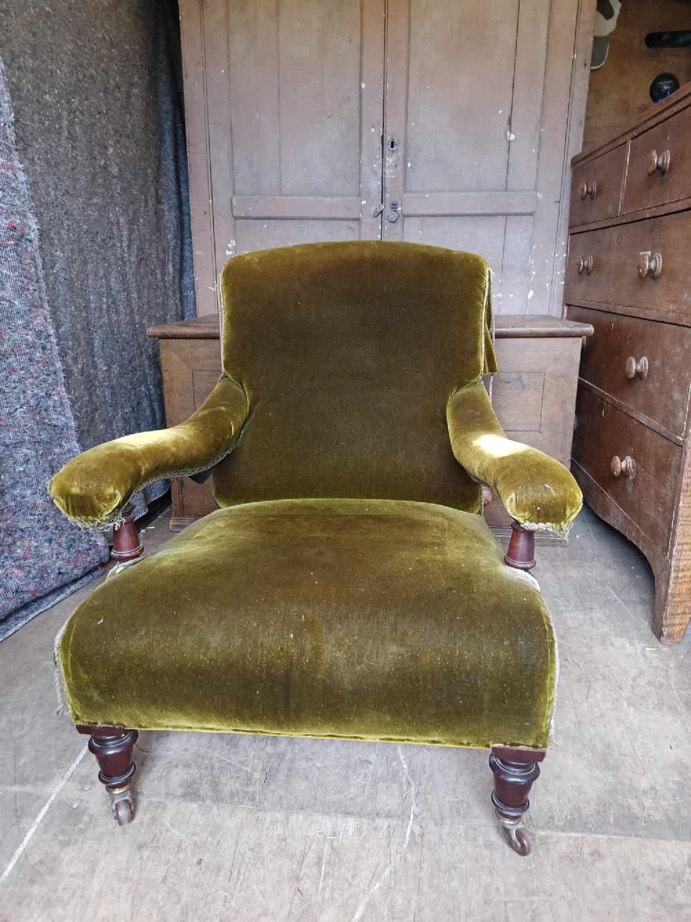 An antique Victorian low easy chair upholstered in olive green velvet with turned wooden arm supports and legs on brass castors. View III