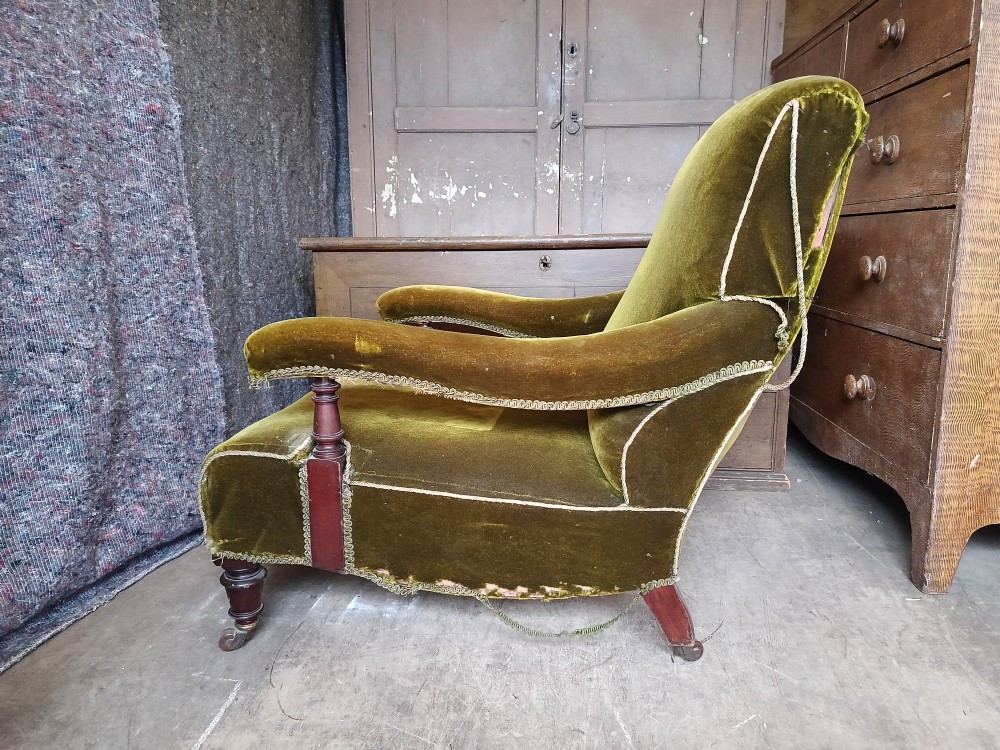 An antique Victorian low easy chair upholstered in olive green velvet with turned wooden arm supports and legs on brass castors. View IV