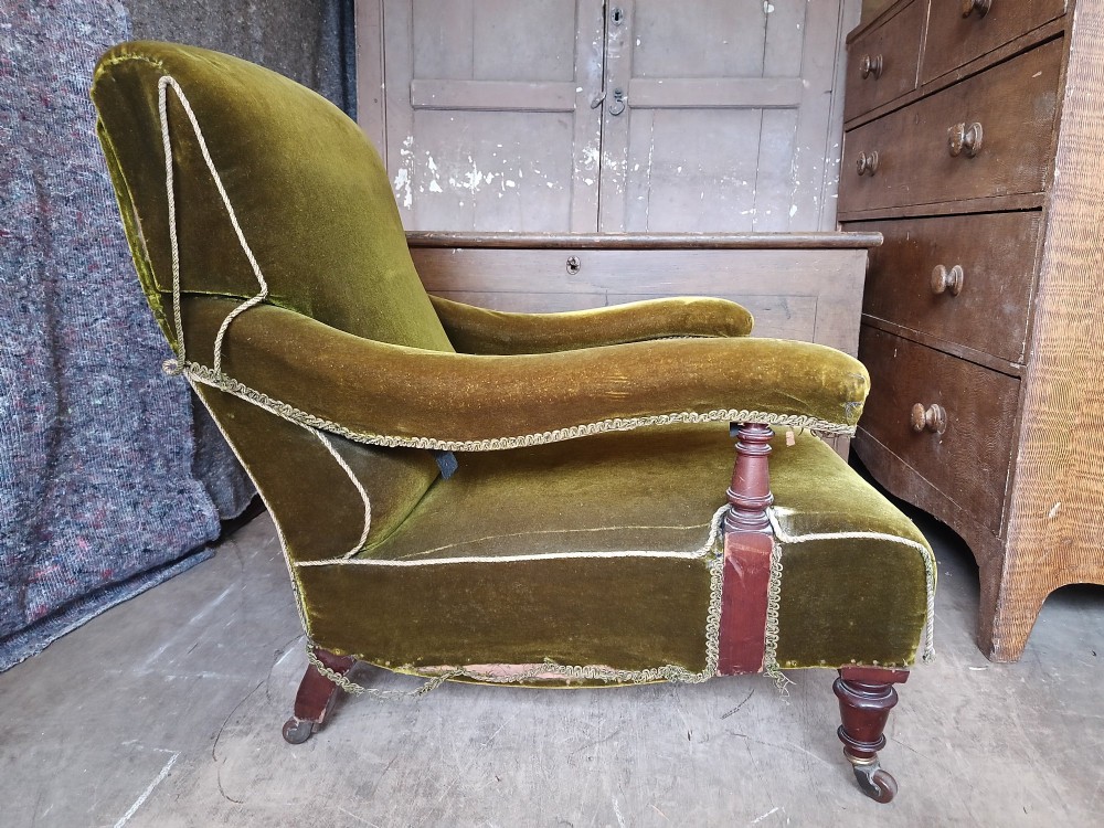 An antique Victorian low easy chair upholstered in olive green velvet with turned wooden arm supports and legs on brass castors. View V