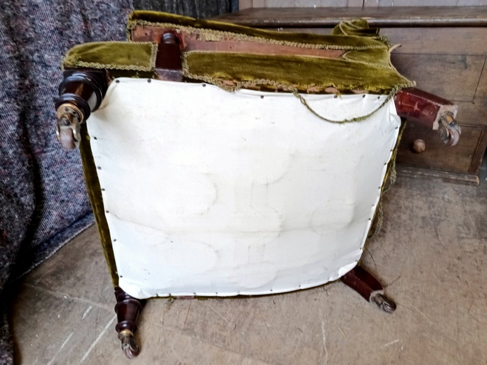 An antique Victorian low easy chair upholstered in olive green velvet with turned wooden arm supports and legs on brass castors. View VII