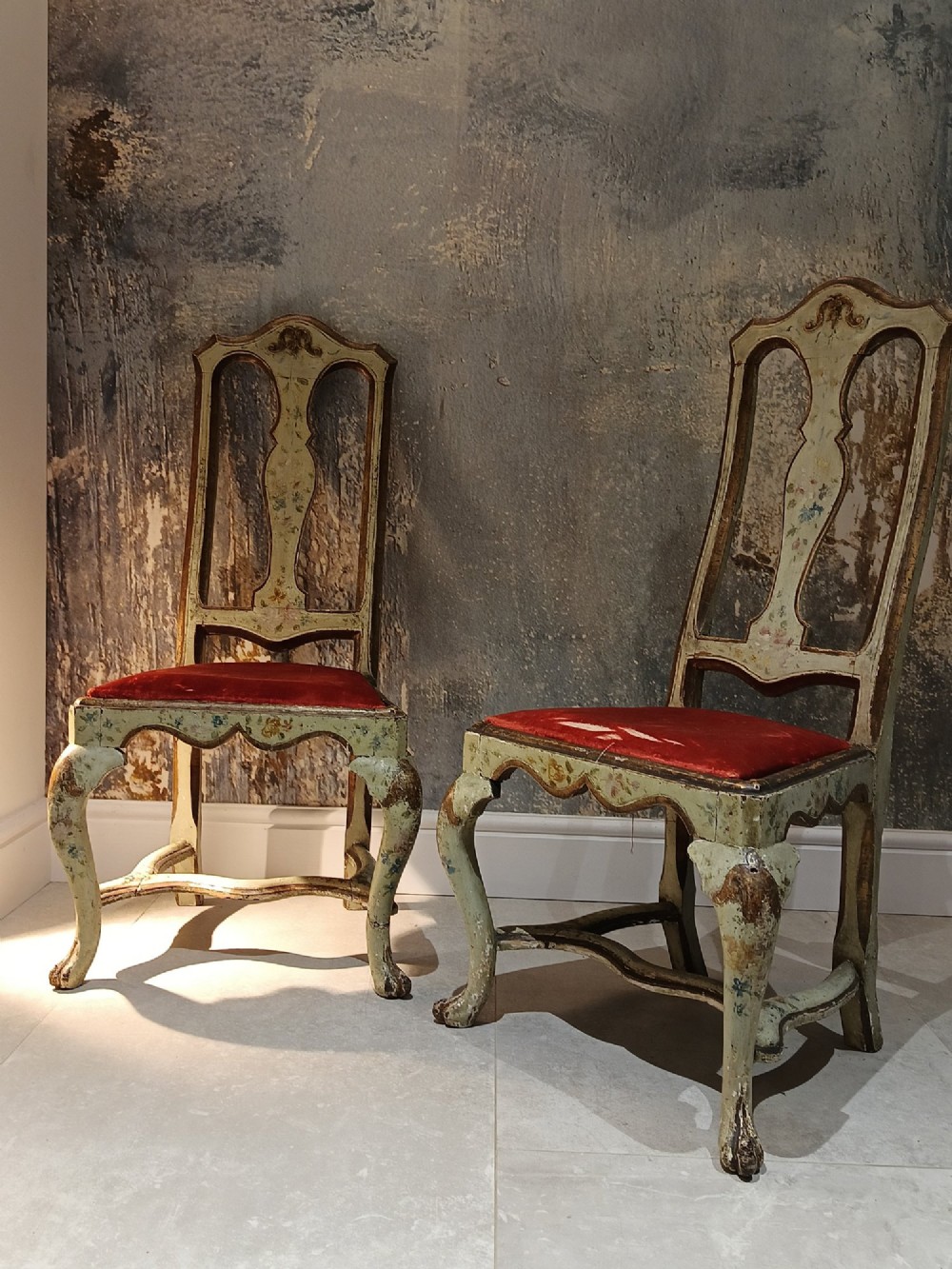 A pair of 18th-century North Italian side chairs featuring distressed cream painted frames with carved crests, cabriole legs, and red velvet seats. View II