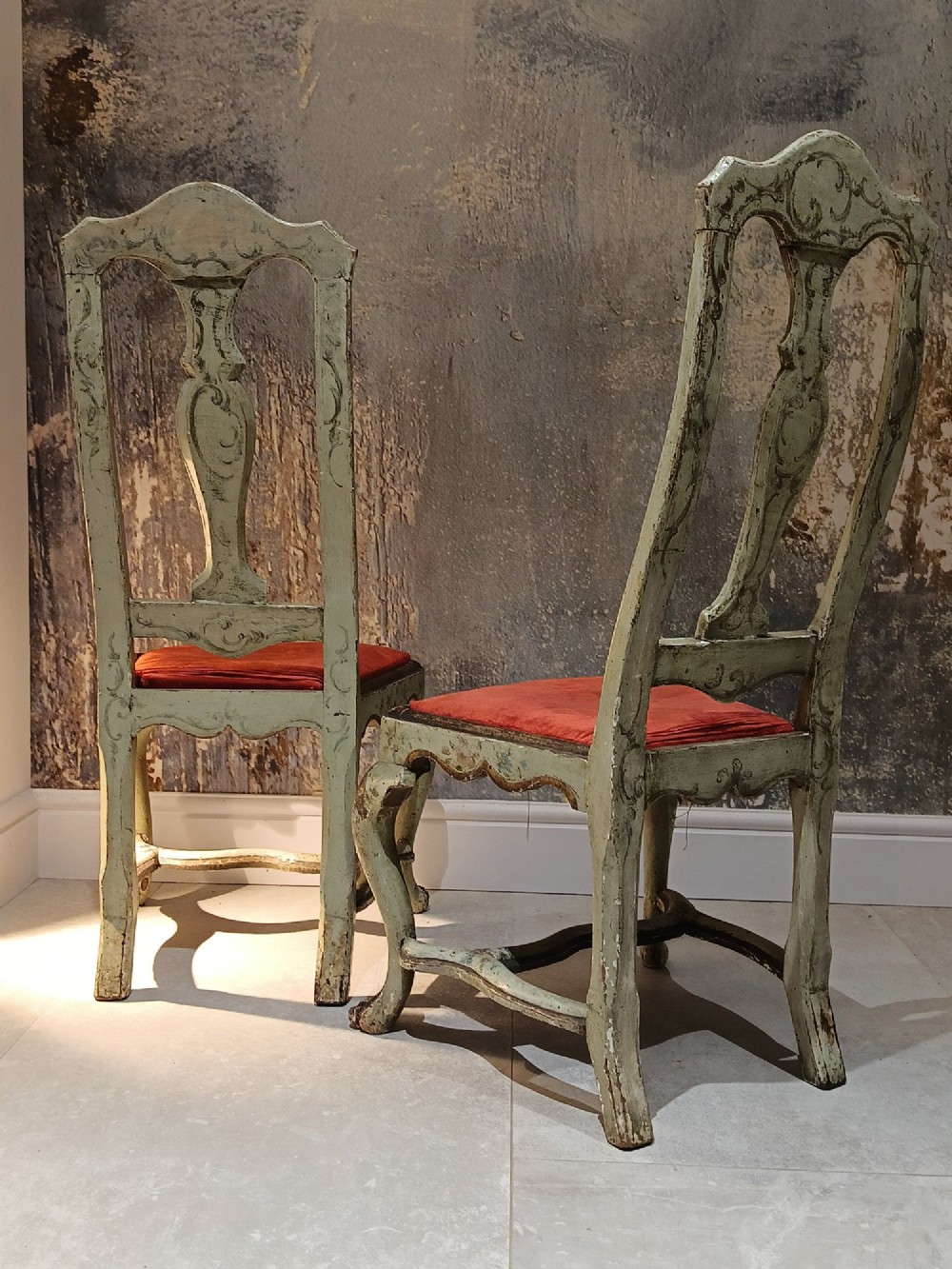 A pair of 18th-century North Italian side chairs featuring distressed cream painted frames with carved crests, cabriole legs, and red velvet seats. View IX