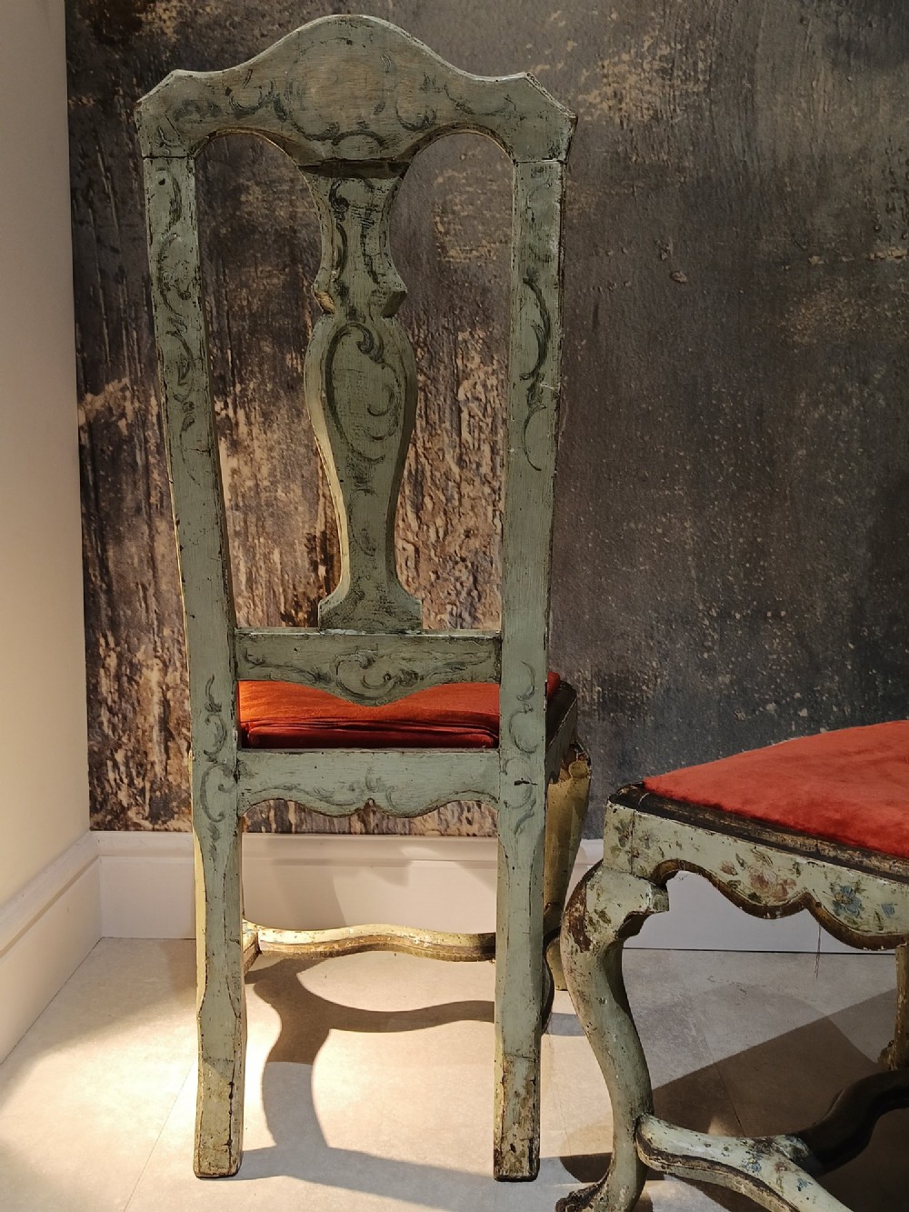 A pair of 18th-century North Italian side chairs featuring distressed cream painted frames with carved crests, cabriole legs, and red velvet seats. View X