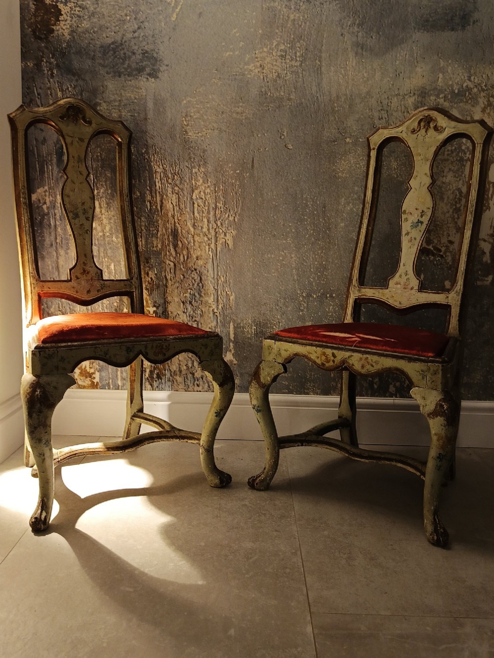 A pair of 18th-century North Italian side chairs featuring distressed cream painted frames with carved crests, cabriole legs, and red velvet seats. View XIV