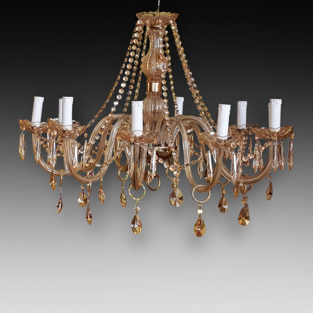A 12-arm amber cut glass chandelier featuring candle-style sockets, glass scroll arms, and suspended crystal teardrop droplets.