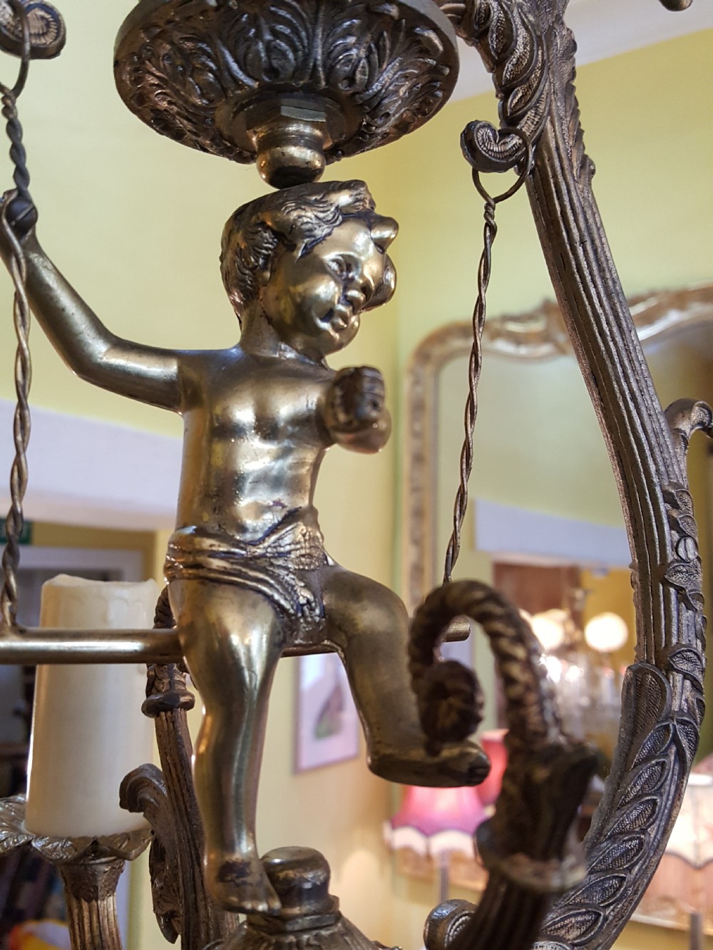 A pair of gilt metal ceiling chandeliers featuring a central figure of a cherub seated on a swing within an ornate lyre-shaped frame with two candle arms. View V
