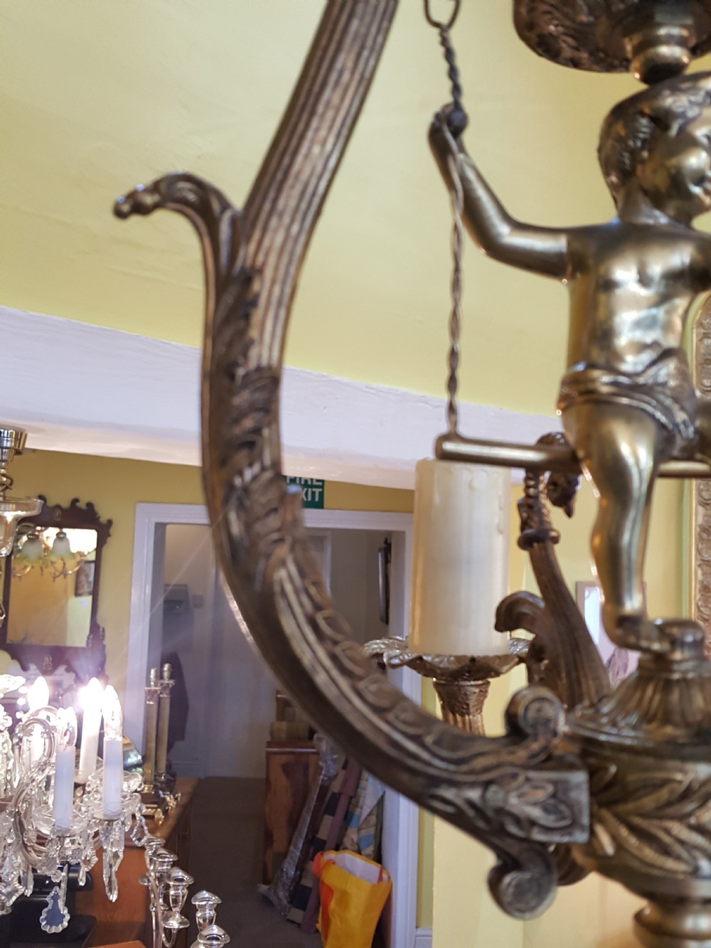 A pair of gilt metal ceiling chandeliers featuring a central figure of a cherub seated on a swing within an ornate lyre-shaped frame with two candle arms. View VIII