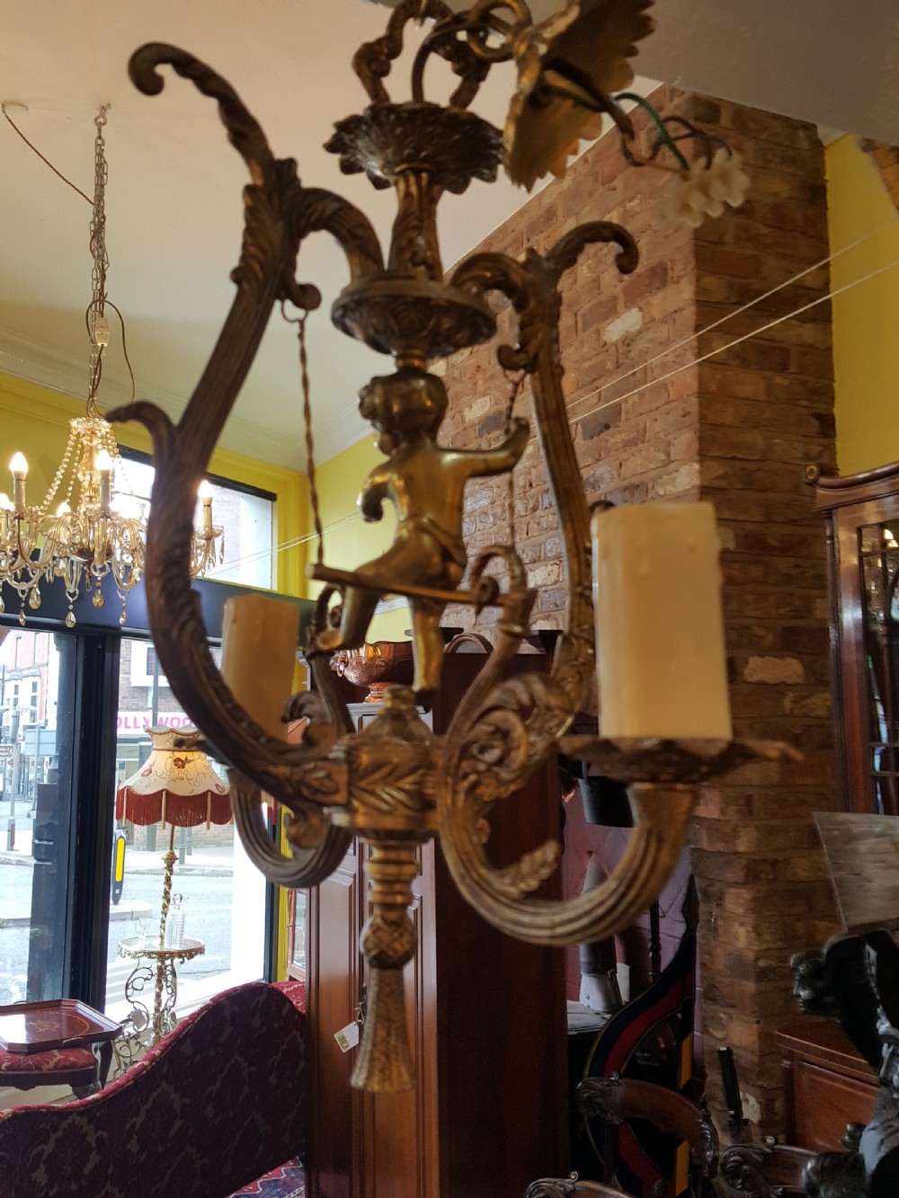 A pair of gilt metal ceiling chandeliers featuring a central figure of a cherub seated on a swing within an ornate lyre-shaped frame with two candle arms. View X