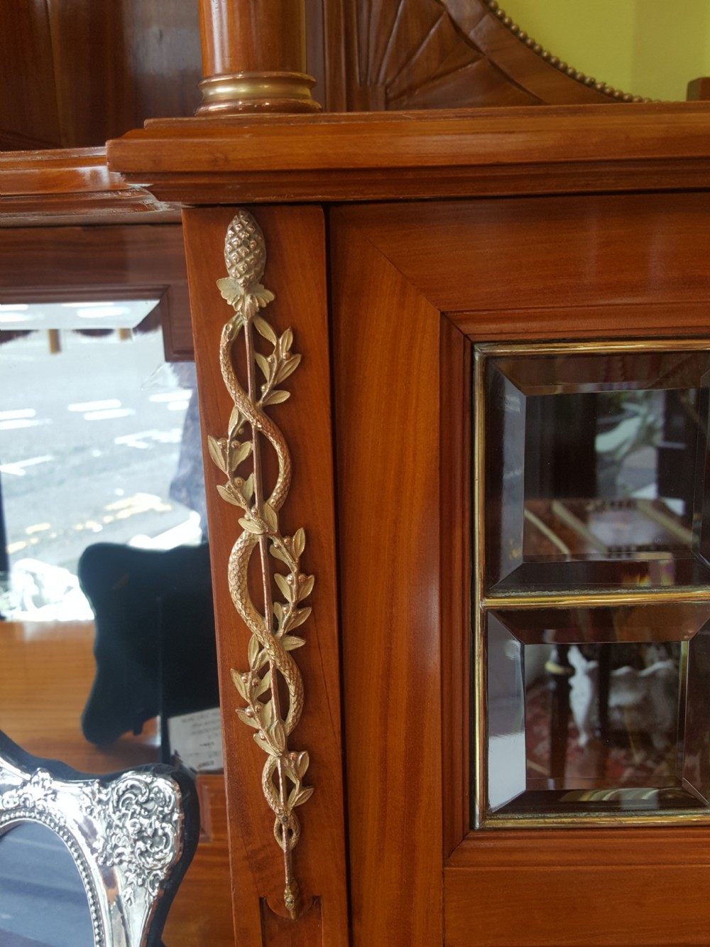 A tall late 19th-century Swiss satinwood salon cabinet featuring a pediment top, gilded metal mounts, glazed display compartments, central mirror, and inlaid door panels. View VIII