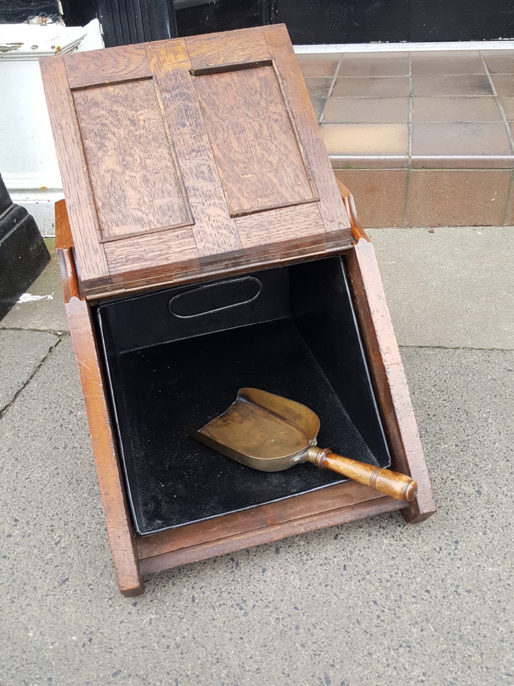 A late Victorian solid oak coal scuttle featuring a slanted panelled front, brass top carrying handle, and rear wooden shovel. View III