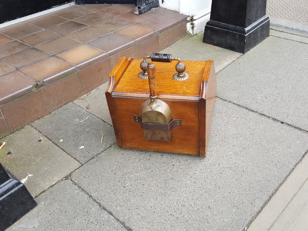 A late Victorian solid oak coal scuttle featuring a slanted panelled front, brass top carrying handle, and rear wooden shovel. View IV