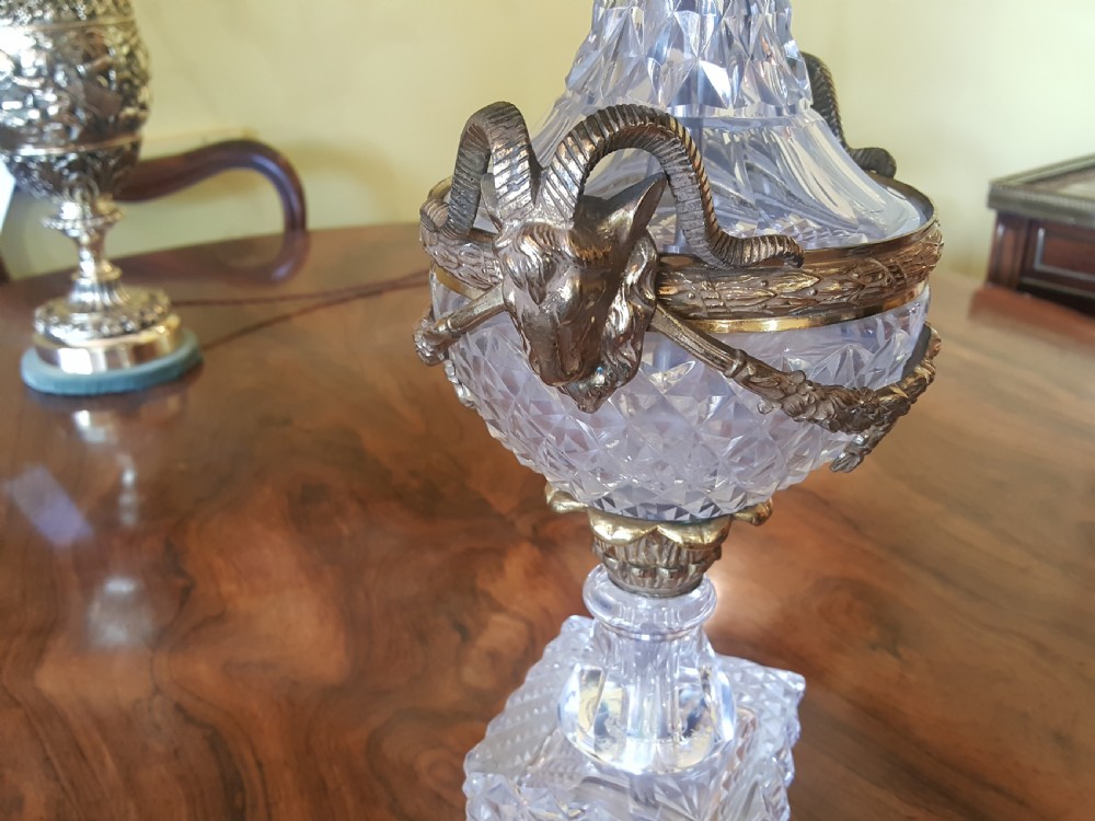 A cut glass urn-form table lamp with ornate gilt metal handles and base, topped with a black and gold patterned domed shade featuring long black fringe trim. View IV