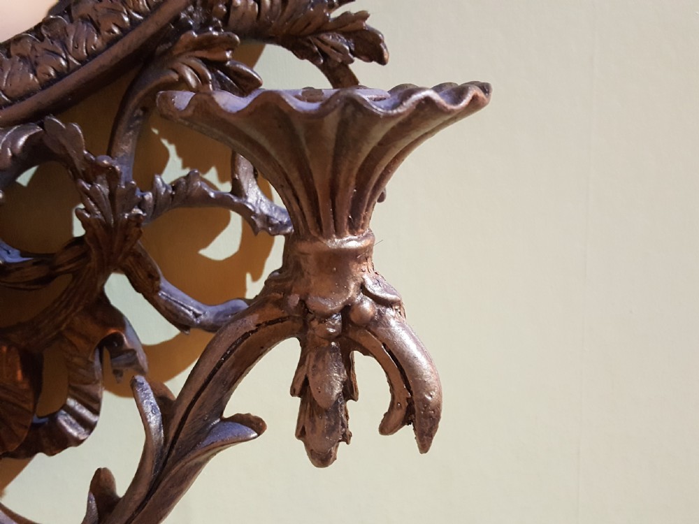An ornate oval giltwood girandole mirror featuring carved acanthus cresting, ribbon detailing, and two candle sconces at the base. View II