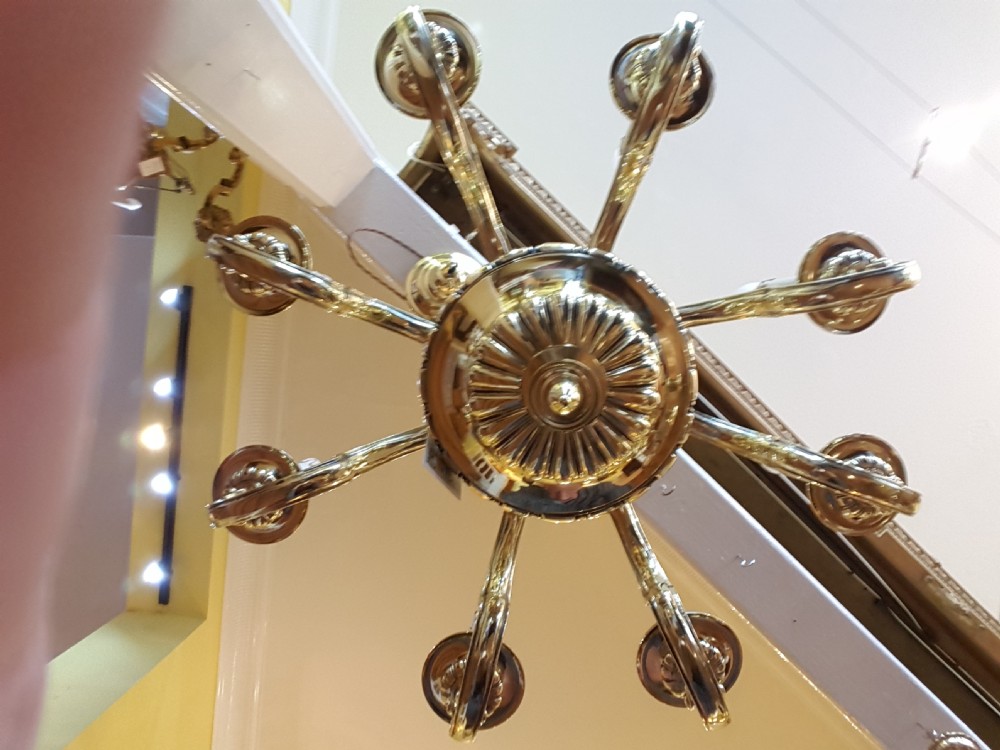 An early twentieth-century brass chandelier featuring eight S-scroll arms surrounding a turned central baluster stem with candle sleeves. View II