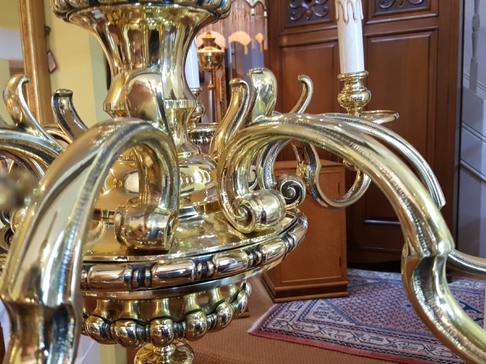 An early twentieth-century brass chandelier featuring eight S-scroll arms surrounding a turned central baluster stem with candle sleeves. View V