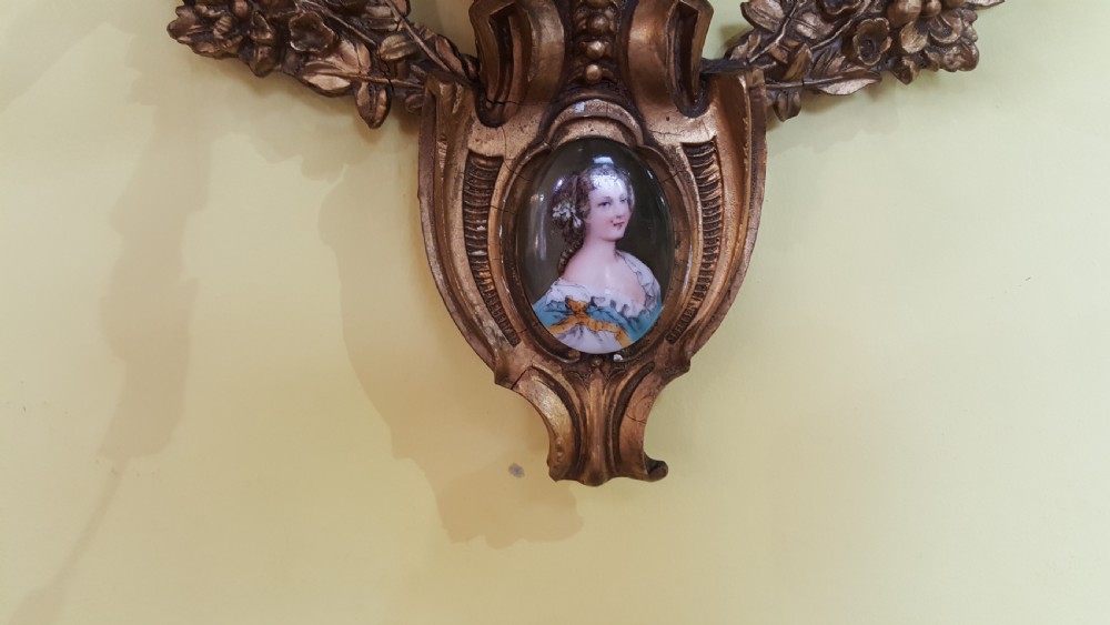 A 19th-century oval giltwood wall mirror featuring an ornate shell cresting, candle sconces at the base, and an inset miniature portrait. View II