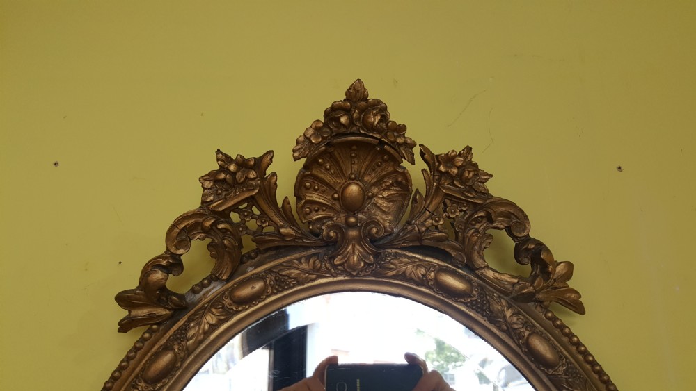 A 19th-century oval giltwood wall mirror featuring an ornate shell cresting, candle sconces at the base, and an inset miniature portrait. View IV