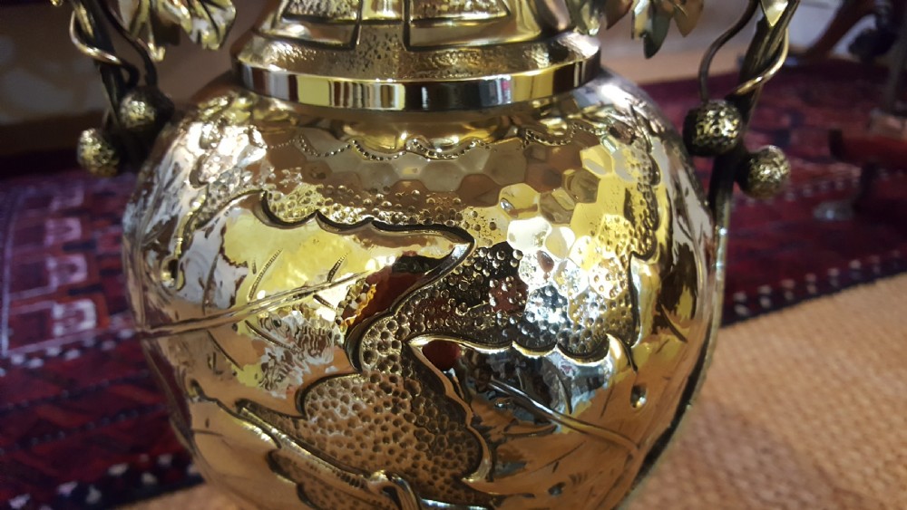 An Art Nouveau brass table lamp shaped like an urn with foliate handles and an intricate patterned fabric shade with decorative fringe. View V