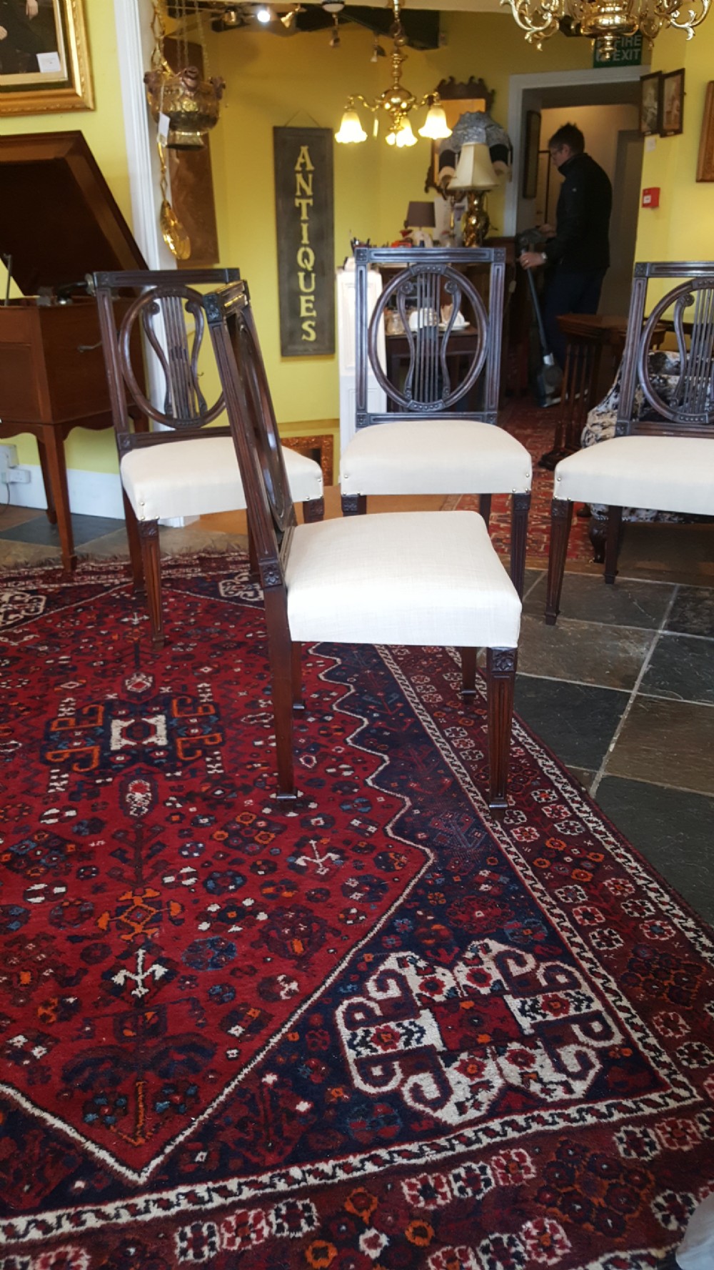 A set of four Regency mahogany side chairs featuring carved lyre back splats inside circular frame apertures, with off-white upholstered seats and fluted front legs. View VI
