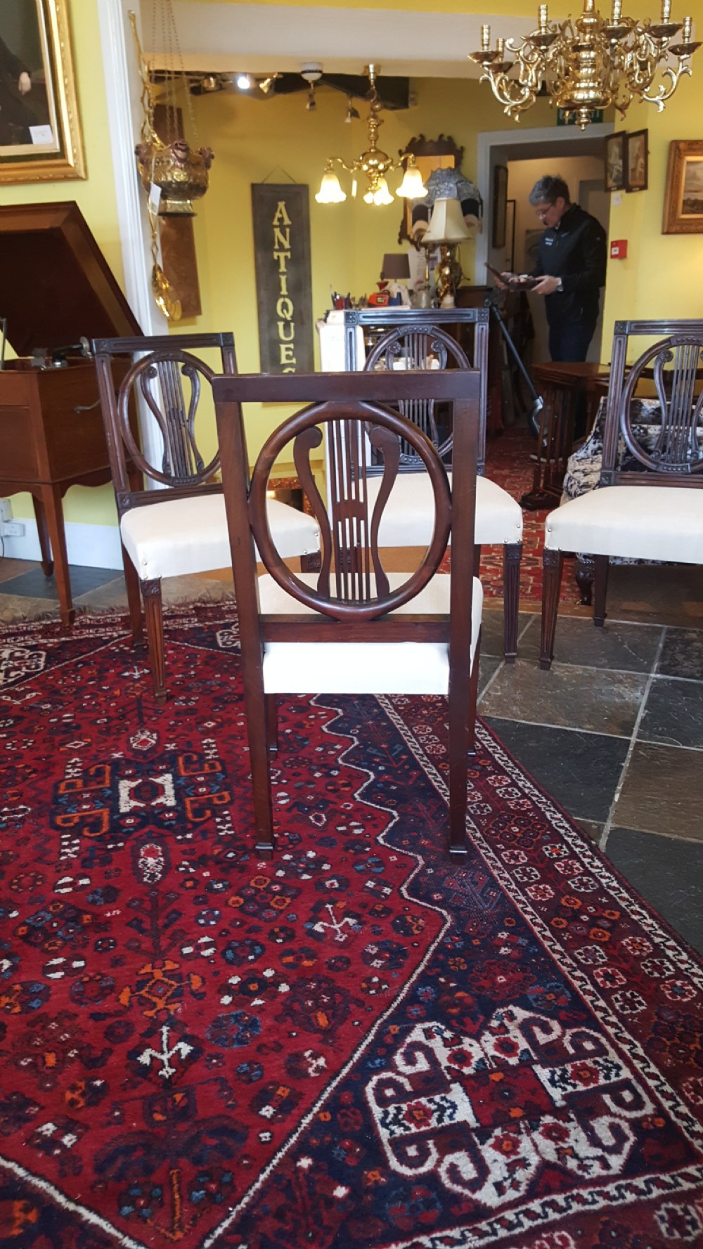 A set of four Regency mahogany side chairs featuring carved lyre back splats inside circular frame apertures, with off-white upholstered seats and fluted front legs. View VII