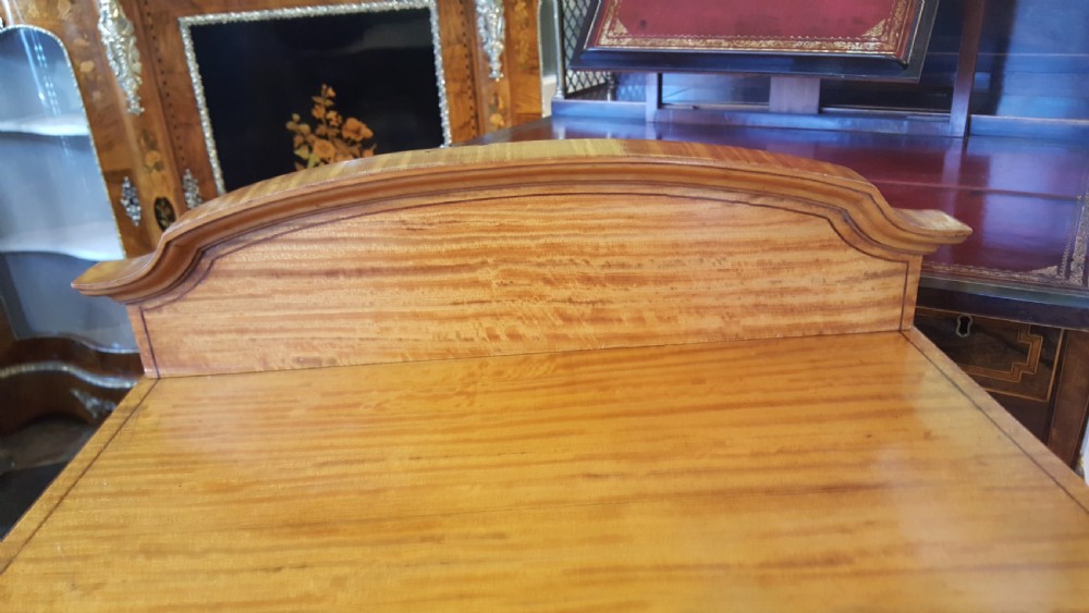An antique Sheraton Revival satinwood bow-fronted bedside cabinet featuring a top drawer above a single cupboard door with geometric parquetry on square tapered legs. View IV